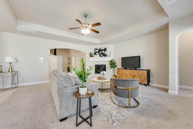 living room featuring ceiling fan, light colored carpet, a fireplace, and a tray ceiling