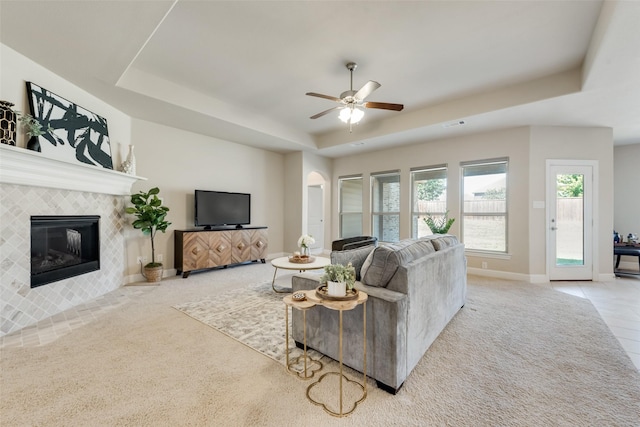 carpeted living room with a fireplace, a tray ceiling, and ceiling fan