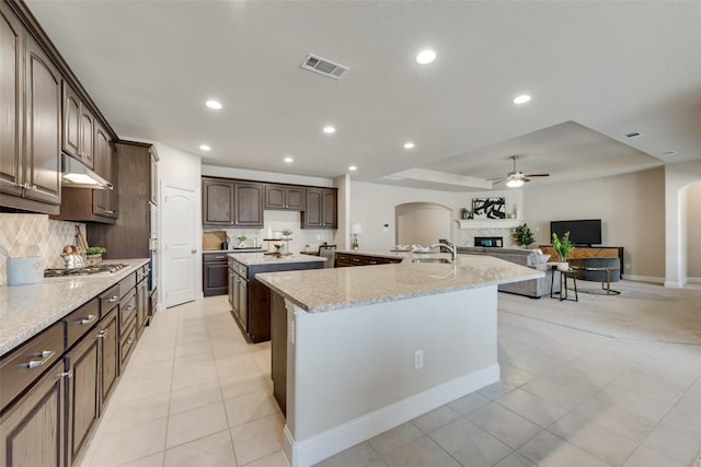 kitchen featuring tasteful backsplash, sink, stainless steel gas cooktop, a kitchen island with sink, and dark brown cabinetry