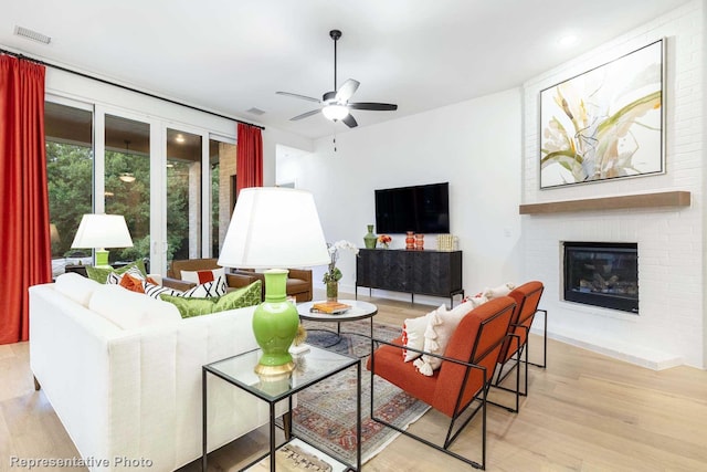 living room featuring ceiling fan, a fireplace, and light hardwood / wood-style flooring