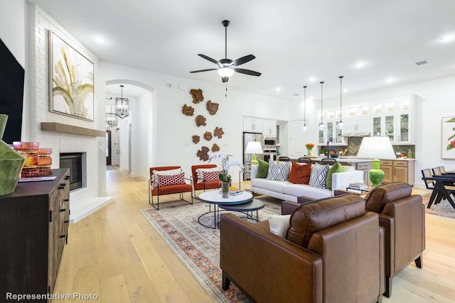 living room featuring a brick fireplace, ceiling fan with notable chandelier, and light hardwood / wood-style floors