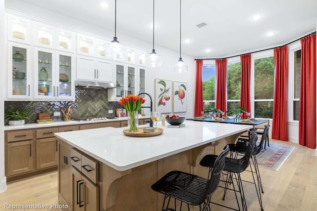 kitchen with stainless steel gas stovetop, tasteful backsplash, a center island with sink, and white cabinets