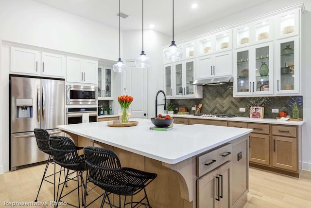 kitchen with pendant lighting, stainless steel appliances, tasteful backsplash, an island with sink, and white cabinets