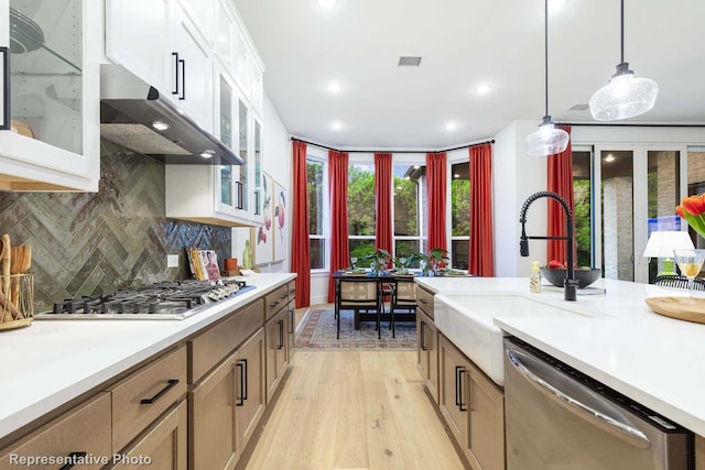 kitchen featuring tasteful backsplash, white cabinetry, hanging light fixtures, stainless steel appliances, and light wood-type flooring