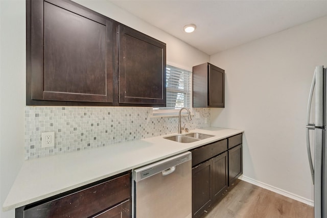 kitchen with backsplash, dark brown cabinets, stainless steel appliances, sink, and light hardwood / wood-style flooring