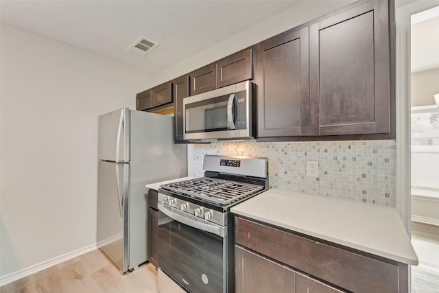 kitchen with dark brown cabinetry, stainless steel appliances, light hardwood / wood-style flooring, and backsplash