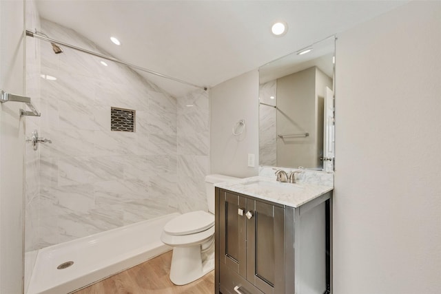 bathroom featuring hardwood / wood-style flooring, vanity, toilet, and a tile shower