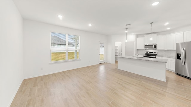 kitchen with a center island with sink, white cabinets, appliances with stainless steel finishes, hanging light fixtures, and light stone countertops