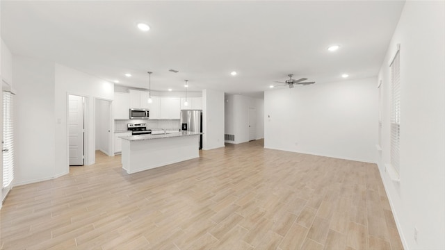 kitchen featuring a center island, decorative light fixtures, stainless steel appliances, open floor plan, and white cabinetry