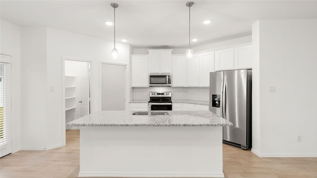 kitchen featuring a kitchen island with sink, hanging light fixtures, light stone countertops, appliances with stainless steel finishes, and white cabinetry