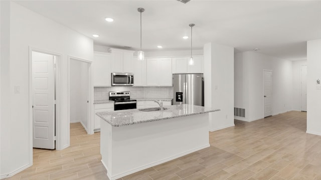 kitchen with stainless steel appliances, visible vents, white cabinetry, a sink, and an island with sink