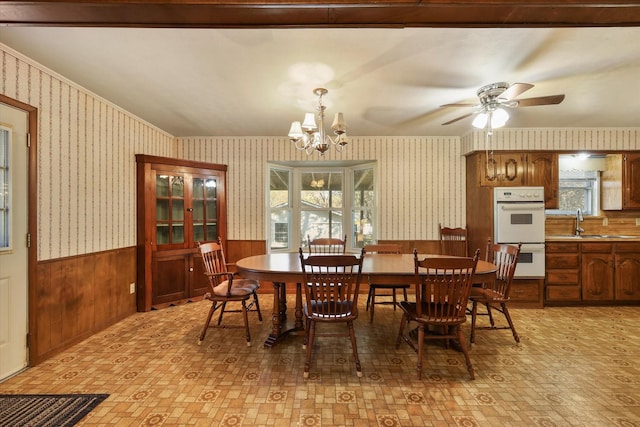 dining room featuring ceiling fan with notable chandelier, sink, and wooden walls