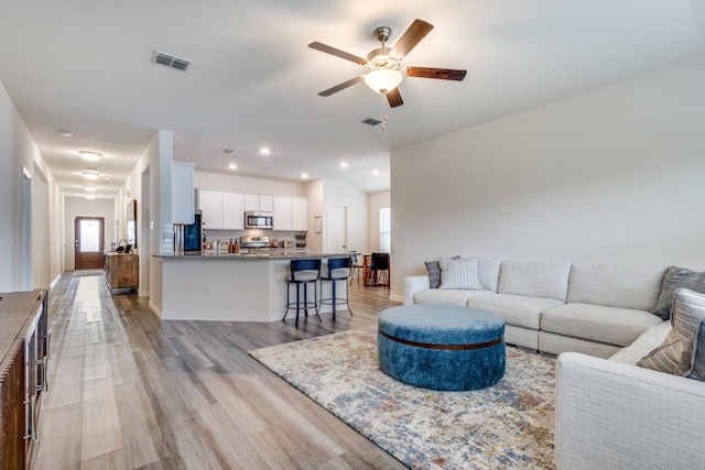 living room featuring ceiling fan, light wood-type flooring, a wealth of natural light, and vaulted ceiling