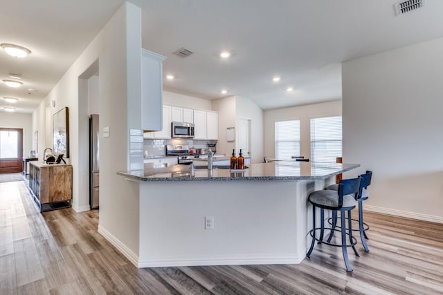 kitchen with tasteful backsplash, stainless steel appliances, stone countertops, light hardwood / wood-style floors, and white cabinetry