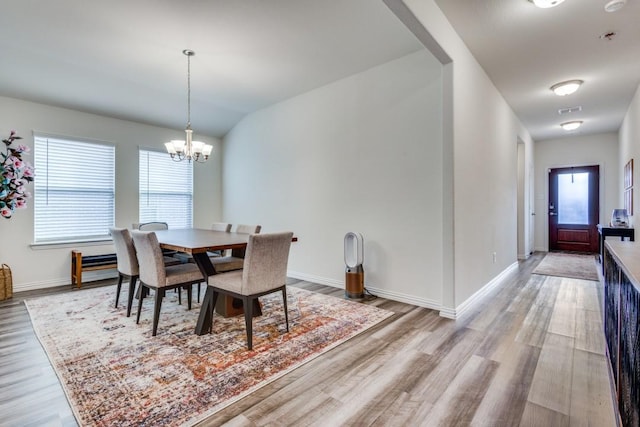 dining space featuring light hardwood / wood-style floors, vaulted ceiling, and a notable chandelier