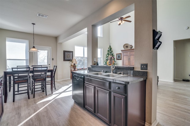 kitchen with black dishwasher, sink, hanging light fixtures, dark brown cabinetry, and light hardwood / wood-style floors