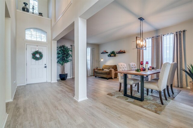 dining room with a towering ceiling, light hardwood / wood-style floors, and ceiling fan with notable chandelier