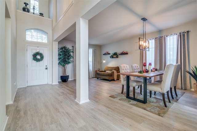 dining room featuring a towering ceiling, a notable chandelier, and light hardwood / wood-style flooring