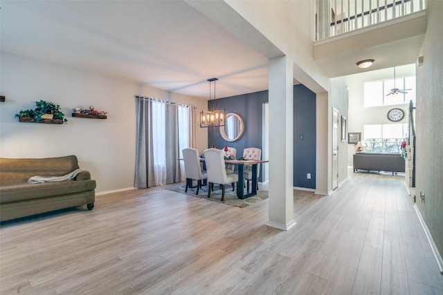 dining area with an inviting chandelier, light hardwood / wood-style flooring, a healthy amount of sunlight, and a high ceiling