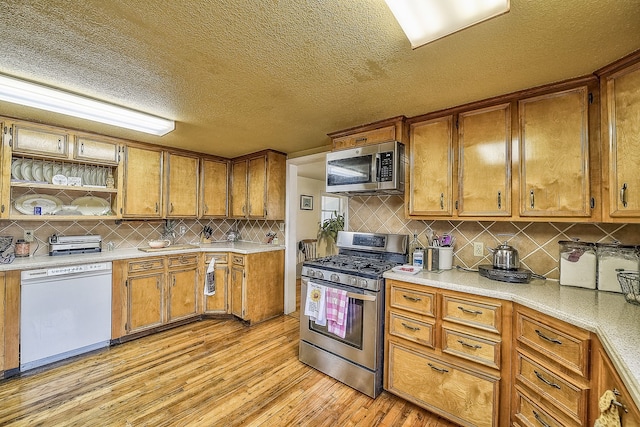 kitchen featuring appliances with stainless steel finishes, light wood-type flooring, tasteful backsplash, and a textured ceiling