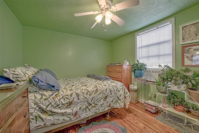 bedroom featuring a textured ceiling, light hardwood / wood-style flooring, ceiling fan, and cooling unit