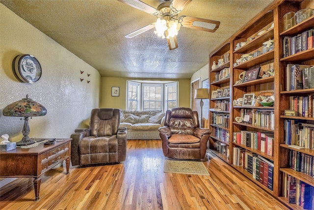 living area featuring ceiling fan, vaulted ceiling, a textured ceiling, and light hardwood / wood-style flooring