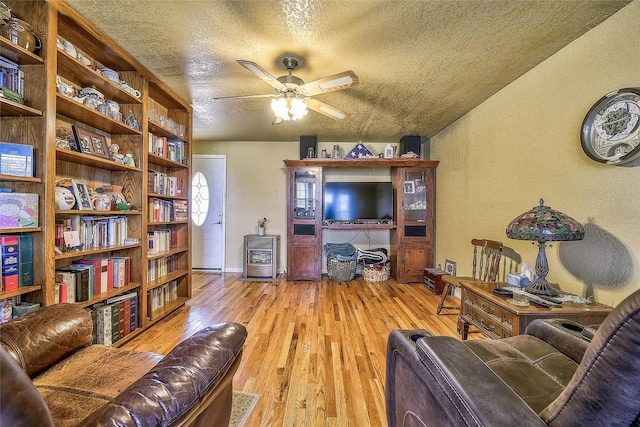 living room with ceiling fan, a textured ceiling, and light wood-type flooring