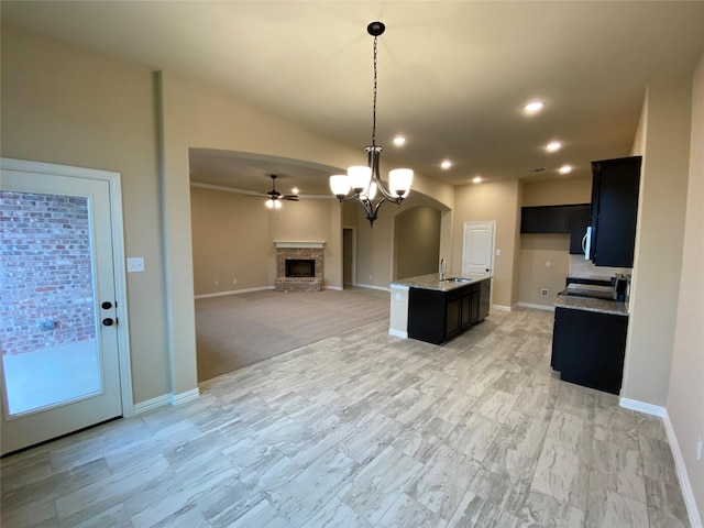 kitchen featuring a center island with sink, ceiling fan with notable chandelier, sink, vaulted ceiling, and light stone counters