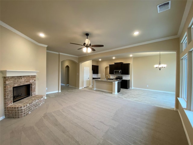 unfurnished living room with sink, a brick fireplace, crown molding, light colored carpet, and ceiling fan with notable chandelier