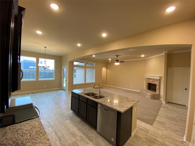 kitchen with a fireplace, ceiling fan with notable chandelier, sink, dishwasher, and an island with sink