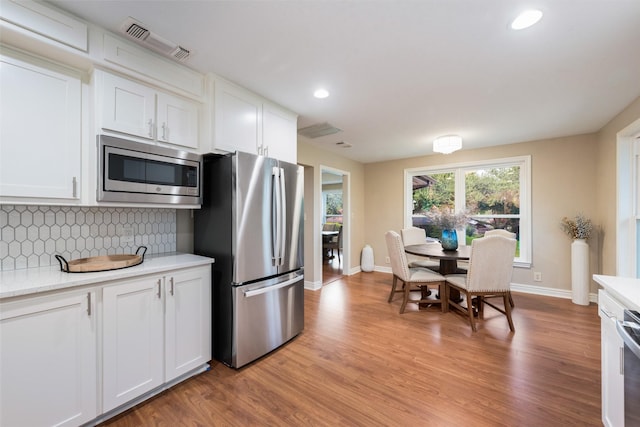 kitchen with decorative backsplash, white cabinetry, stainless steel appliances, and light hardwood / wood-style flooring