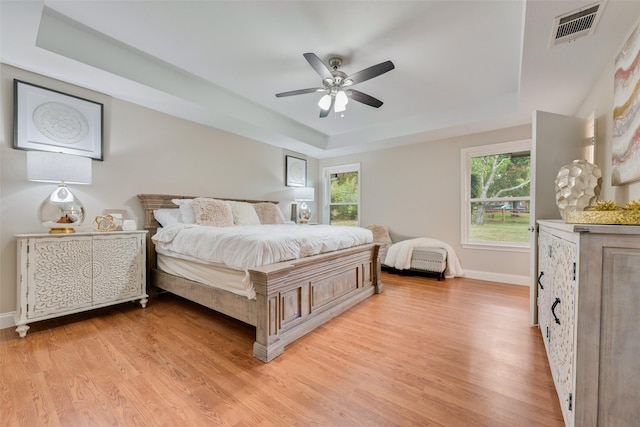 bedroom featuring ceiling fan, light wood-type flooring, multiple windows, and a tray ceiling