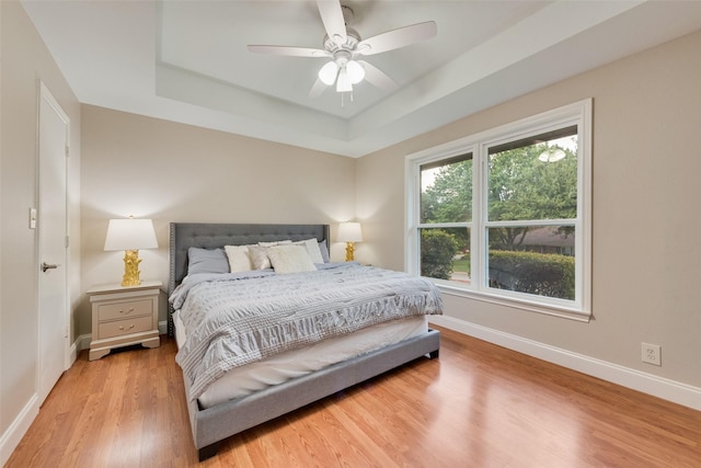 bedroom with a raised ceiling, ceiling fan, and light hardwood / wood-style flooring