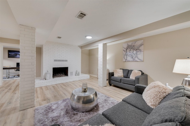 living room with light hardwood / wood-style floors, a brick fireplace, and decorative columns