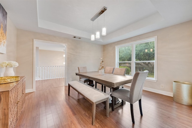 dining area featuring wood-type flooring, a raised ceiling, and a chandelier