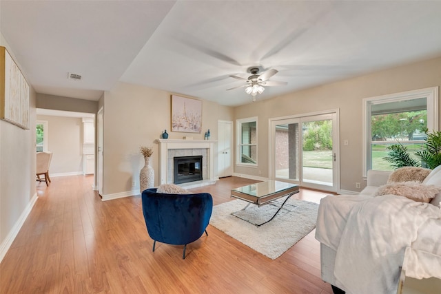 living room with light hardwood / wood-style floors, ceiling fan, and a tiled fireplace