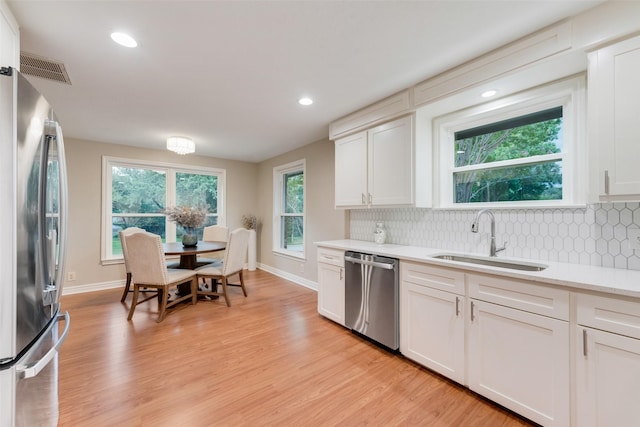 kitchen with sink, appliances with stainless steel finishes, decorative backsplash, white cabinets, and light wood-type flooring