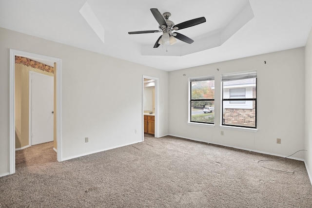 unfurnished bedroom with ceiling fan, ensuite bath, a tray ceiling, and carpet