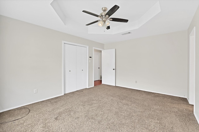 unfurnished bedroom with ceiling fan, a closet, a raised ceiling, and carpet