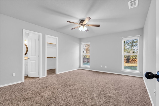 unfurnished bedroom with a spacious closet, ceiling fan, carpet, connected bathroom, and a closet