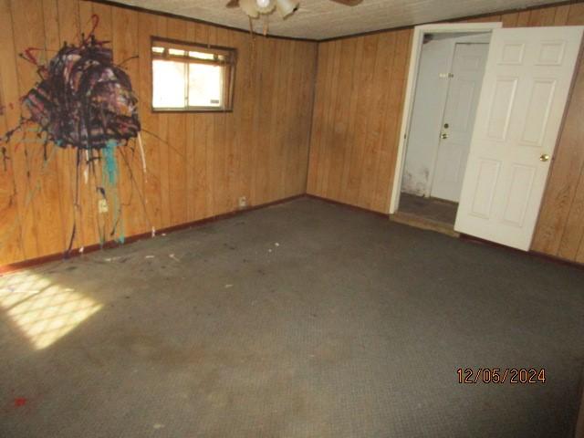 interior space with wooden walls, ceiling fan, and dark carpet