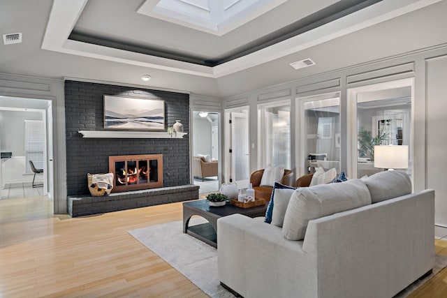 living room with a fireplace, hardwood / wood-style flooring, a raised ceiling, and a healthy amount of sunlight