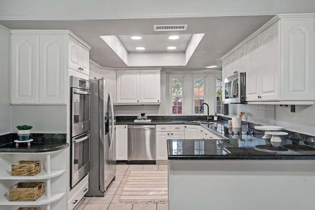 kitchen featuring kitchen peninsula, a raised ceiling, stainless steel appliances, and white cabinets