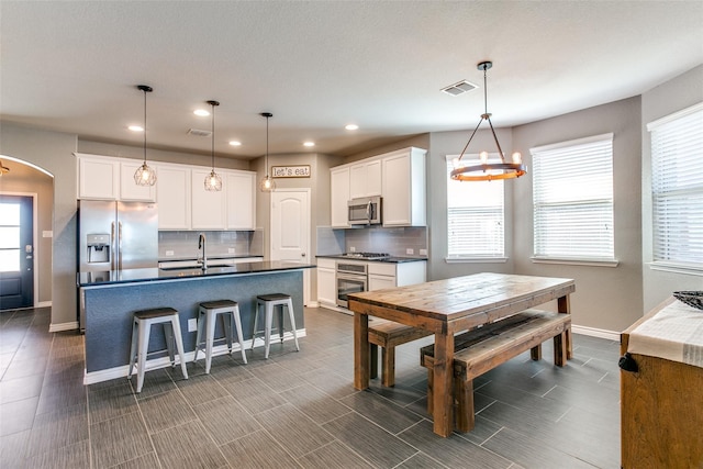 kitchen featuring white cabinets, appliances with stainless steel finishes, hanging light fixtures, and an island with sink