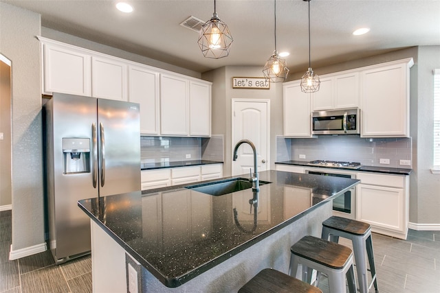 kitchen featuring sink, hanging light fixtures, a kitchen island with sink, white cabinets, and appliances with stainless steel finishes