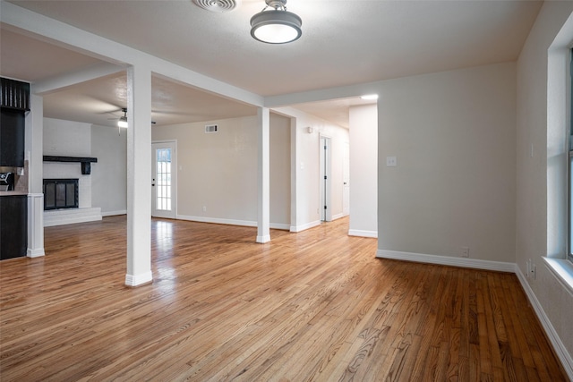 unfurnished living room with ceiling fan, light wood-type flooring, and a brick fireplace