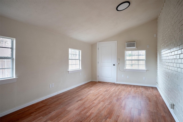 spare room with a wealth of natural light, light hardwood / wood-style flooring, brick wall, and vaulted ceiling