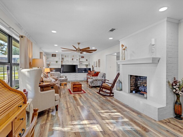 living room with a brick fireplace, ornamental molding, ceiling fan, and light wood-type flooring