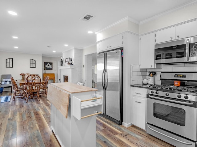 kitchen featuring appliances with stainless steel finishes, hardwood / wood-style floors, white cabinetry, decorative backsplash, and crown molding