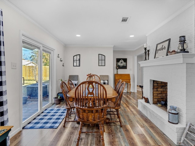 dining space with a fireplace, wood-type flooring, and ornamental molding